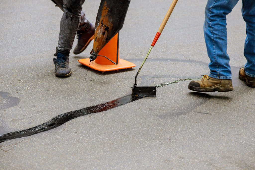 Maintenance crew applying hot-pour sealant with a squeegee to repair an asphalt crack.