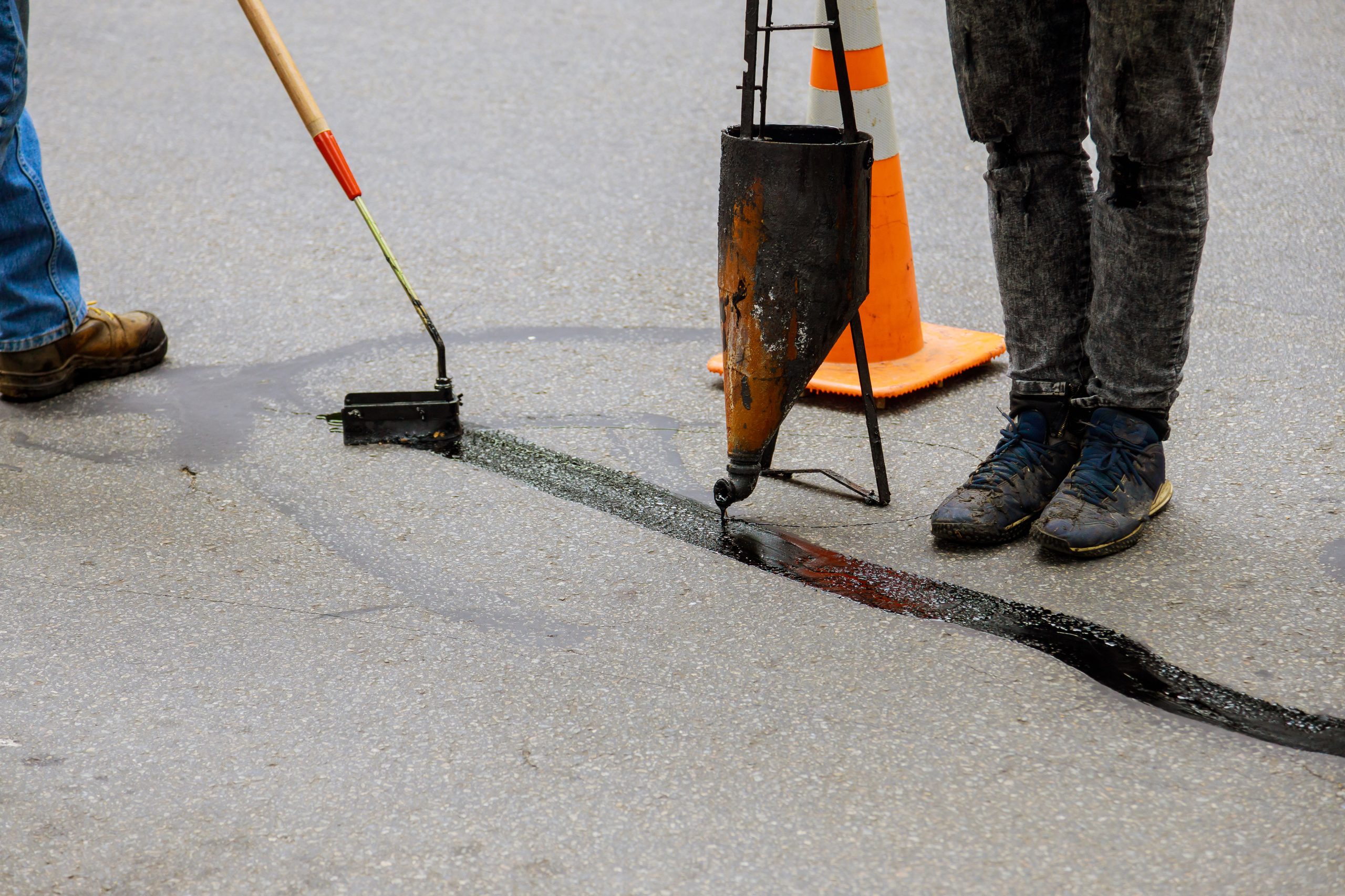 Road crew applying hot-pour sealant to fill an asphalt crack.