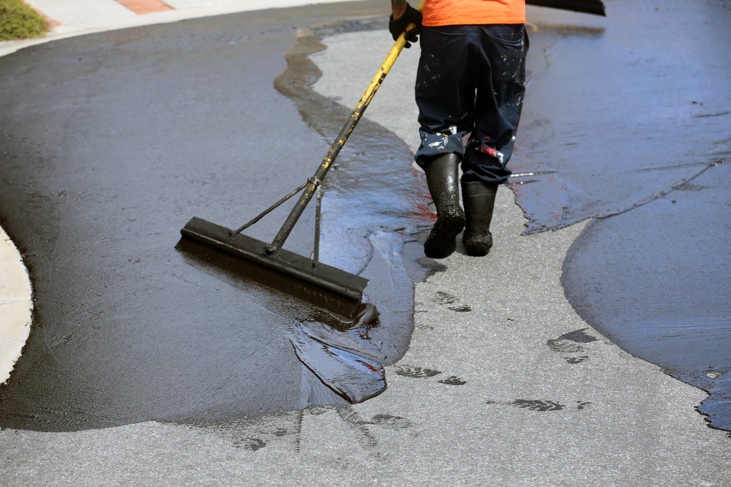 Crew member leveling fresh asphalt with a squeegee during street repair on a residential road.