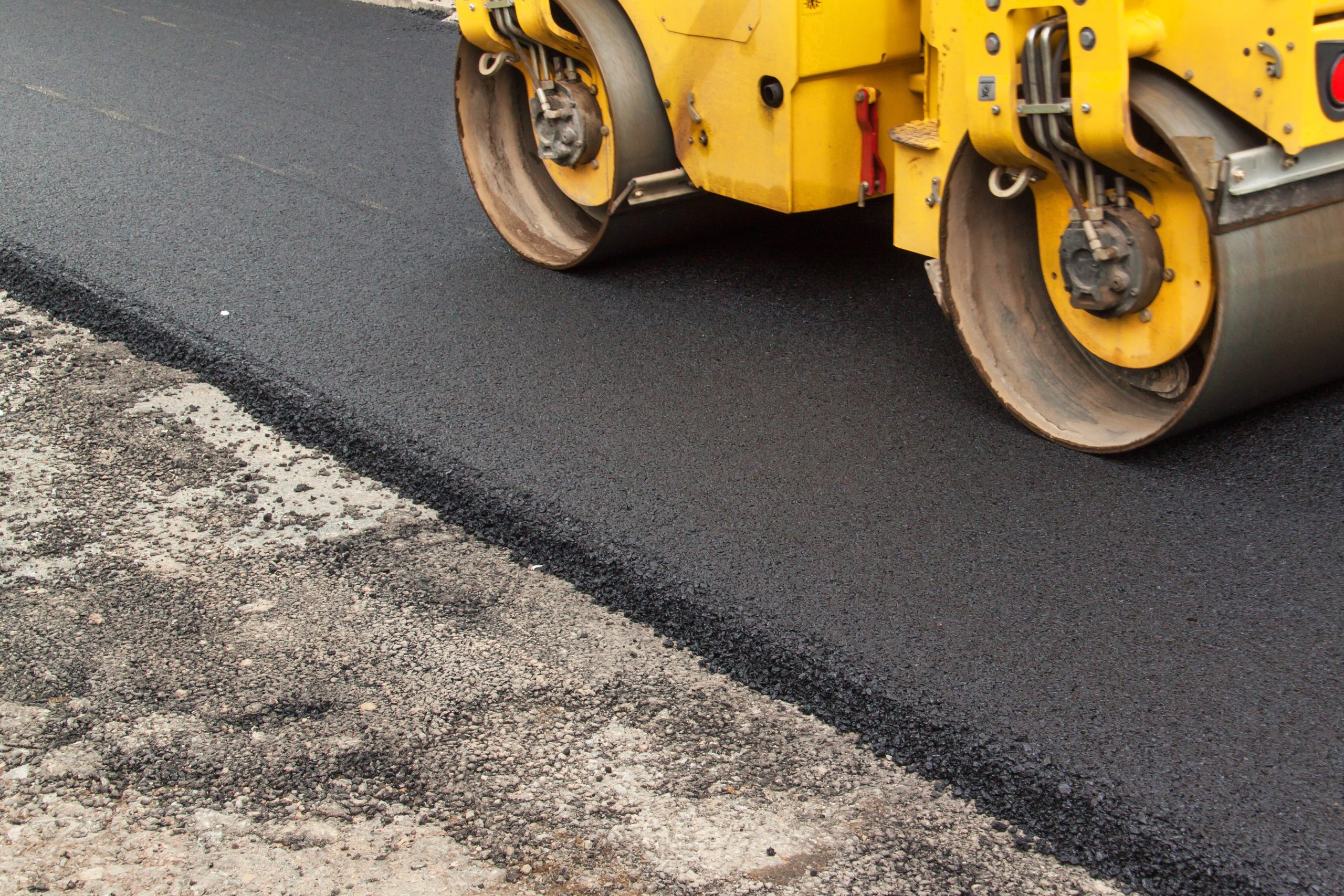 Steamroller compacting freshly laid asphalt during new road paving construction.