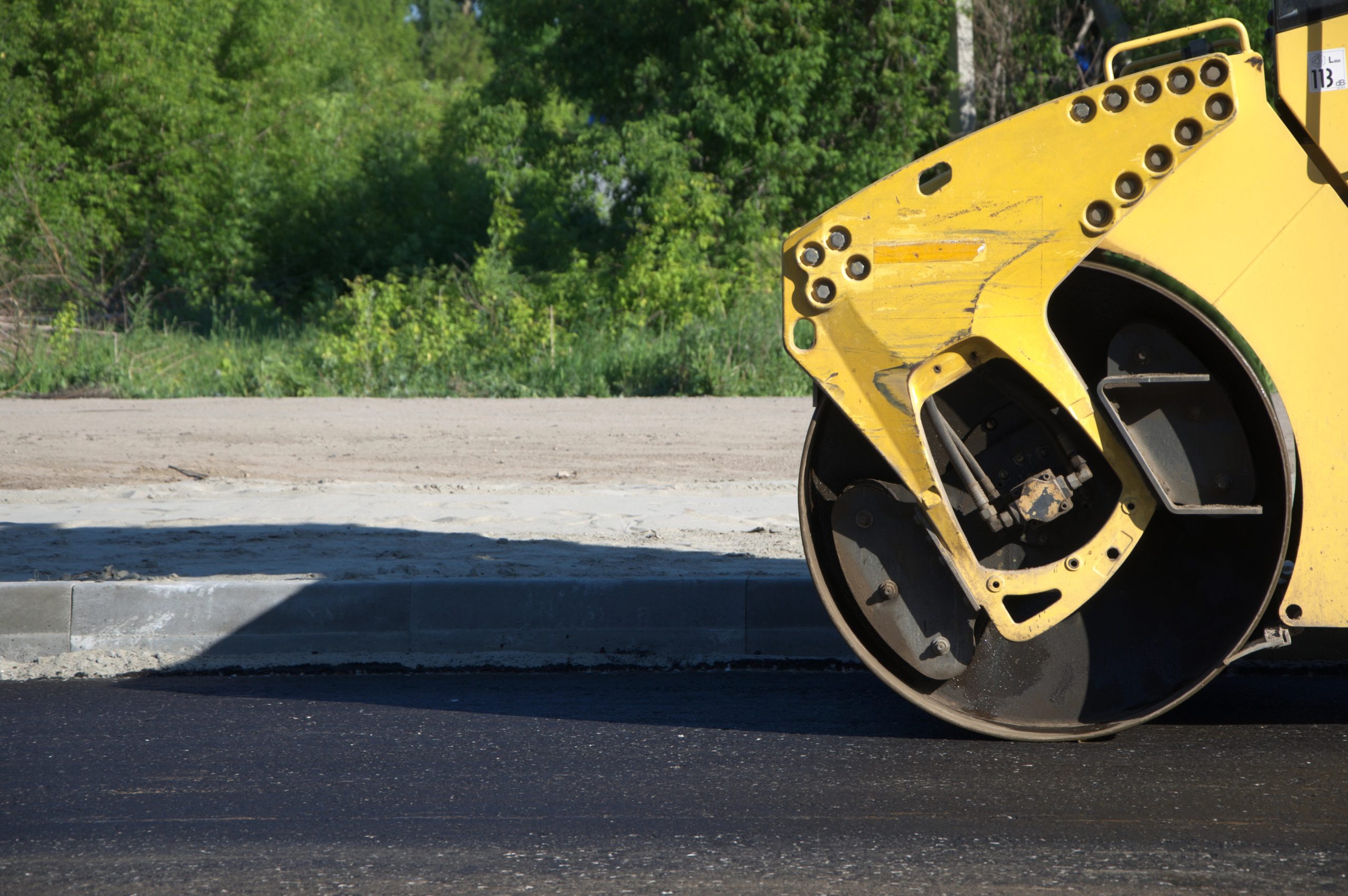 Close-up of steamroller compacting new asphalt road near curb during paving project.