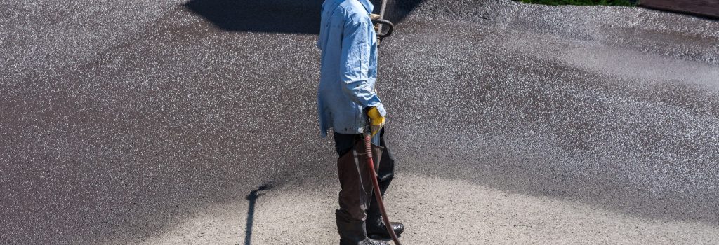Worker applying asphalt sealcoat to residential driveway with spray hose for surface protection and restoration.