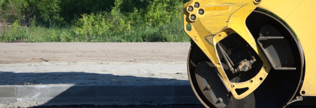 Close-up of steamroller compacting new asphalt road near curb during paving project.